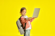 © Ilshat - Sweet asin ethnicity school girl child holding laptop, have a backpack on her shoulders, learning from home remotely, preparing homework online, stands over yellow isolated background.
