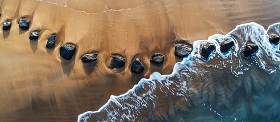 Aufkleber - Aerial view of a meandering line of black stones on a sandy beach, providing ample copy space for an image.