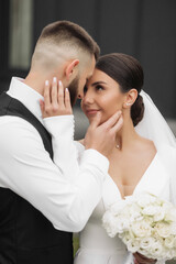 Wall Mural - A bride and groom are embracing each other with their hands on their faces. The bride is wearing a white dress and the groom is wearing a black vest