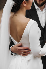 Wall Mural - A bride and groom are posing for a picture. The bride is wearing a white dress and a veil, while the groom is wearing a black suit. The couple is embracing each other