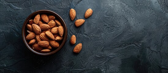 Poster - Almonds in a dark wooden bowl on a slate table for healthy diet concept with available copy space image.