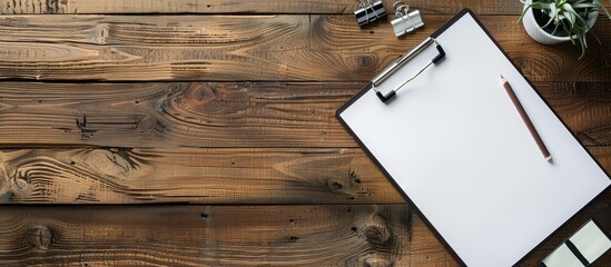 Poster - Aerial view of a wooden desk with a white clipboard holding blank paper, along with a pen, pencil, and clips. Ample space available for text or images.