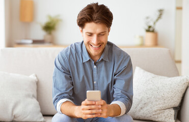 Poster - A man sits on a couch, smiling and looking at his phone.