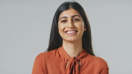 Wall Mural - Head and shoulders studio portrait of smiling young Indian businesswoman against grey background wearing business suit looking at camera - shot in slow motion