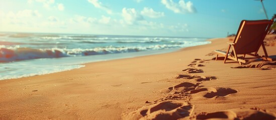 Wall Mural - A beach landscape on a sunny day with footprints in the sand and a lounge chair. A focused shot of the sand with a blurred sea and sky background on a summer day, offering copy space for an image.