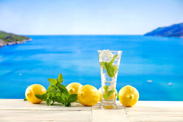 Sticker - Glass of fresh icy lemonade with mint leaves on wooden  table and copy space for drinks and food and products. Seascape in summer background.