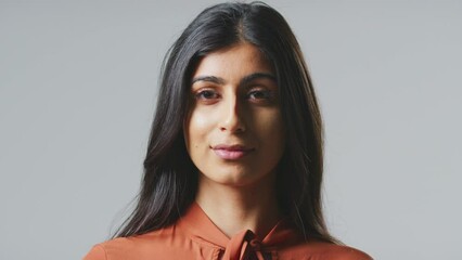 Wall Mural - Head and shoulders studio portrait of serious looking young Indian businesswoman against grey background wearing business suit turning to look at camera - shot in slow motion