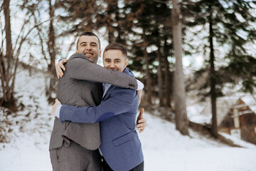 Wall Mural - Two men hug each other in the snow. One of them is wearing a blue jacket. Scene is warm and friendly