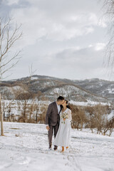 Wall Mural - A couple is kissing in the snow, with a beautiful mountain in the background. The bride is wearing a white dress and the groom is wearing a suit