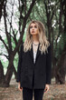 © angel_nt - Young woman with blonde dreadlocks stands in a wooded area, wearing a black blazer and looking up