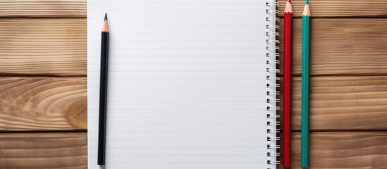 Poster - A white notebook with a metal spiral and three colorful ballpoint pens (green, red, and blue) are arranged on a wooden table, symbolizing office work, back to school, and stationery, presenting a