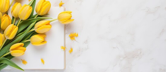 Poster - Top view arrangement of fresh yellow tulips on a marble surface with a notepad and sketchbook, providing copy space in a delightful spring-themed image.