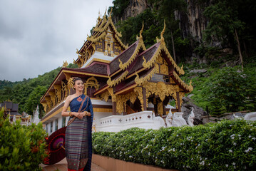 Wall Mural - Woman wearing Thai dress visits beautiful temple in Thailand.