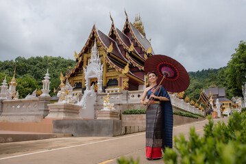 Wall Mural - Woman wearing Thai dress visits beautiful temple in Thailand.