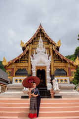 Wall Mural - Woman wearing Thai dress visits beautiful temple in Thailand.