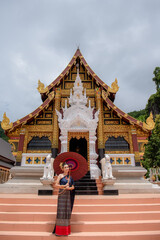 Wall Mural - Woman wearing Thai dress visits beautiful temple in Thailand.