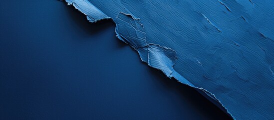 Fototapete - Solid deep blue background with a sheet of textured blue craft paper turned over, seen from above, creating a visually appealing copy space image.