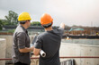 © skarie - Team of construction workers discussing project details with blueprint in construction site.