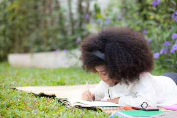 Child lying on mat on grass and drawing on notebook in garden, kid leisure doing activity hobby with drawing artistic in park, education and leisure in summer, education and learning concept.