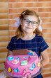 © Irina Schmidt - Little caucasian girl kid celebrating birthday or first day of school holding big cake. Happy smiling school child with pigtails and glasses.