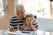 © Irina Schmidt - Cute little baby toddler girl and handsome senior grandfather painting with colorful pencils at home. Grandchild and man having fun together
