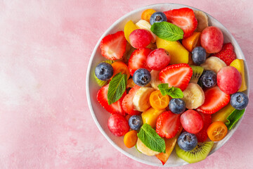 Wall Mural - Healthy fresh fruit salad in a bowl on pink background. Top view with copy space. Summer healthy food for breakfast. Mixed fruits, berries and mint for diet lunch