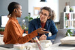 © Mediaphotos - Portrait of smiling young man with long hair listening to female colleague discussing ideas during meeting at workplace in office