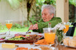 © Brastock Premium - Elderly woman with white hair eating a meal sitting at a table outdoors.