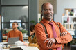 © Mediaphotos - Waist up portrait of confident Black senior man posing in office standing with arms crossed and looking at camera with serious expression copy space