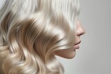 close-up of a young, blonde woman's flowing hair on a gray background. outcome of perming, highlighting, and coloring. Style and beauty