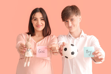 Canvas Print - Young pregnant couple holding toys and papers with sex of baby on pink background