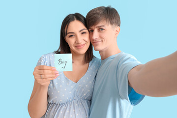 Wall Mural - Young pregnant couple holding paper with word BOY on blue background