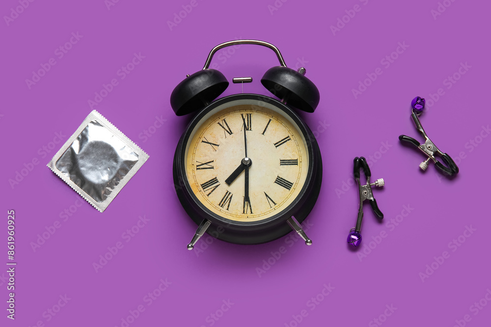 Alarm clock with condom and nipple clamps on purple background. Time for sex