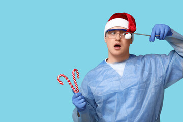 Sticker - Portrait of young male surgeon in Santa hat with candy canes and forceps on blue background