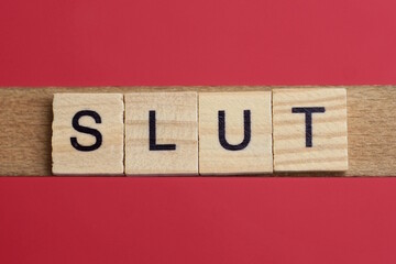 text the word slut from gray wooden small letters with black font on an red table