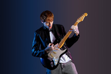 Wall Mural - Cool tattooed young man playing electric guitar on dark background