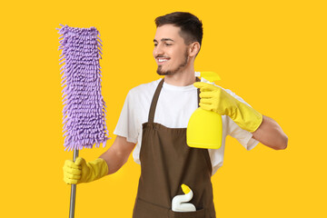 Poster - Male janitor with cleaning spray and mop on yellow background