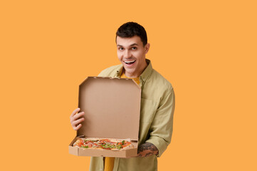Wall Mural - Happy young man holding cardboard box with tasty pizza on yellow background