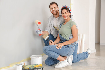 Poster - Beautiful young happy couple with paint roller and brush doing repair in new house