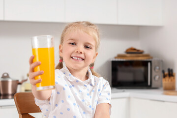 Wall Mural - Cute little girl with glass of orange juice in kitchen