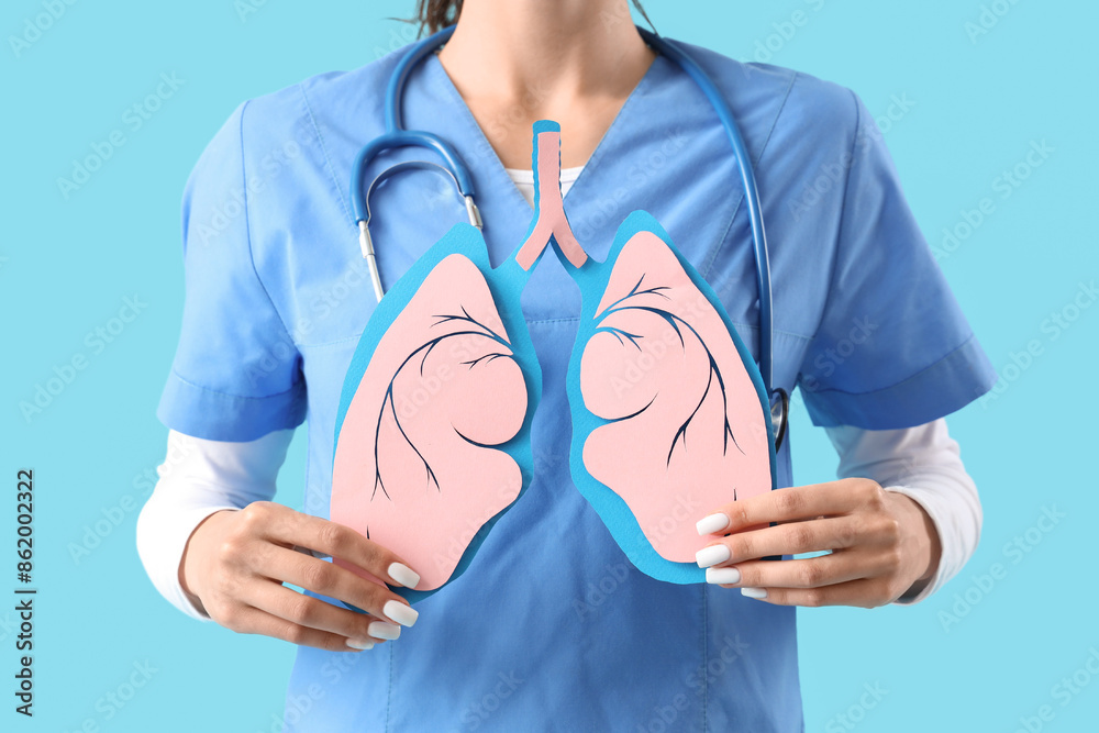 Female doctor with paper lungs on blue background, closeup