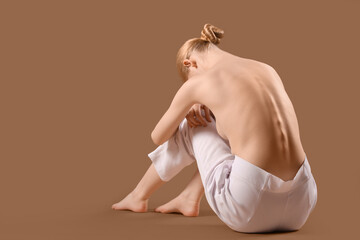 Wall Mural - Beautiful young woman with naked back sitting on brown background