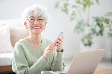 Wall Mural - tapping smiling senior (elderly) woman with computer and smartphone (smart phone) looking at camera 