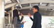 © aFotostock - Two Asian businesspeople talking business partners using digital tablet smartphone talking outside office at street city. Teamwork partnership men talking women at outdoor office partnership team