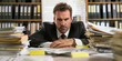 © Юлия Падина - Stressed businessman sitting at his cluttered desk filled with stacks of paperwork in an office, highlighting the concept of workplace stress and overload