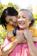 © Wavebreak Media - Asian woman hugging senior mother from behind, both smiling in outdoor setting