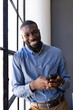 © Wavebreak Media - Smiling businessman holding smartphone, standing by window in office setting