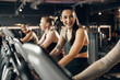 © Flamingo Images - Fit young woman in sportswear laughing while riding on a stationary bike with a group of smiling female friends during a cardio workout session in a gym
