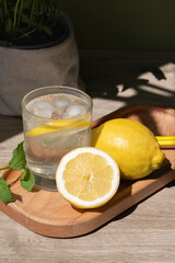 Wall Mural - Authentic natural summer food still life with lemons and glass with lemonade beverage on wooden tray, bright sun light and shadow