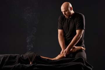 Wall Mural - male masseur doing a massage on a girl's leg on a black background, therapeutic joint massage